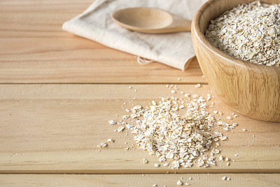 健康食品的概念。旧桌子上的木碗里的燕麦片，背景光线过亮图片下载