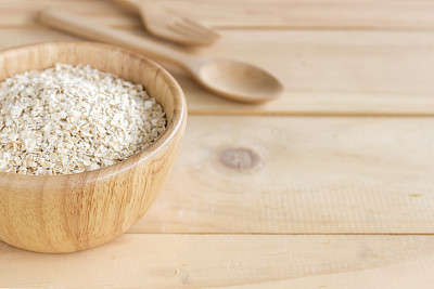 健康食品的概念。旧桌子上的木碗里的燕麦片，背景光线过亮图片下载