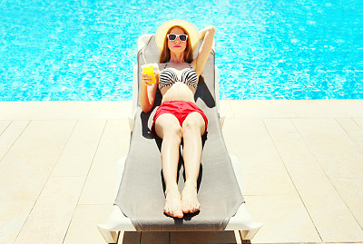 暑假-美丽的女人休息与果汁从杯子上的躺椅在一个蓝色的水池背景图片下载
