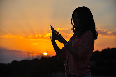 剪影的年轻迷人的嬉皮女孩听着手机音乐和舞蹈在日落图片下载
