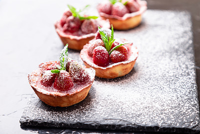 自制草莓挞配糖粉放在板上，黑色背景。关闭了。素材图片