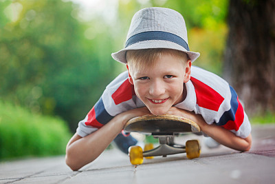 特写照片微笑的男孩在帽子躺在滑板上图片下载