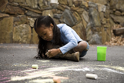 女孩用粉笔在地上画画。图片下载