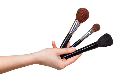 三个化妆笔刷在女性的手近距离孤立的白色。图片下载