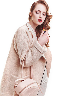 时尚的金发女人穿着漂亮的衣服在工作室摆姿势。穿着大衣，手提包，高跟鞋凉鞋。春天夏天的照片图片下载