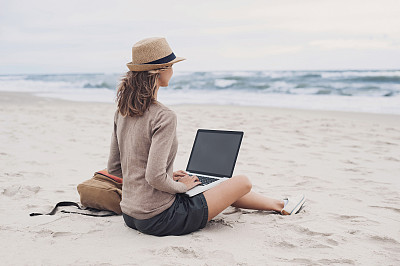 年轻女子在海滩上用笔记本电脑图片下载