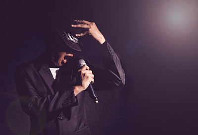 松儿手拿着麦克风，在黑色背景上唱歌，镜头从聚光灯中闪耀，音乐的概念素材图片