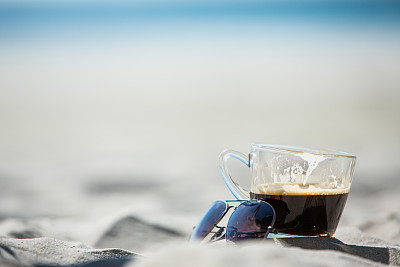 咖啡杯和太阳镜与沙子和海洋背景图片下载