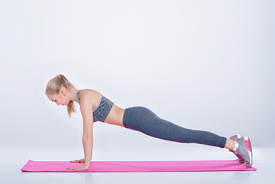 美丽的金发女孩在运动服做运动在健身垫在灰色的背景图片下载