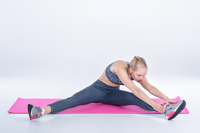 美丽的金发女子在灰色背景的健身垫上做运动。伸展运动图片下载