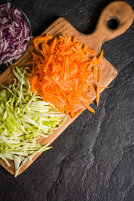 切成薄片的胡萝卜、卷心菜和洋葱放在木板上。黑石的背景。图片下载