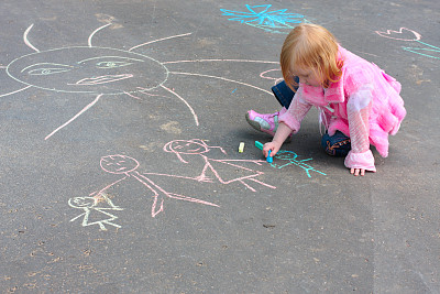 小女孩穿着粉红色的衣服用粉笔在沥青上涂图片下载