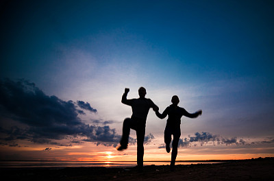 女人和男人的剪影在一个阴天的海滩上的彩色日落背景图片下载