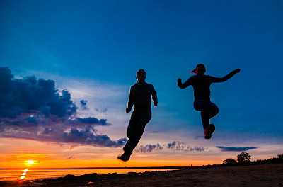 女人和男人的剪影在一个阴天的海滩上的彩色日落背景图片下载