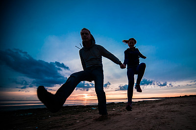 女人和男人的剪影在一个阴天的海滩上的彩色日落背景图片下载