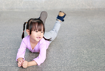 一个快乐可爱的小女孩躺在走廊的地板上。图片下载