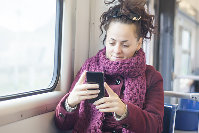 在公共交通工具上微笑并使用手机的女人图片下载