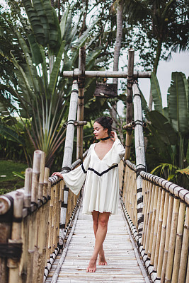 亚洲女孩在巴厘岛乌布的吊桥上行走。豪华别墅围绕苍谷绿色热带花园。图片下载