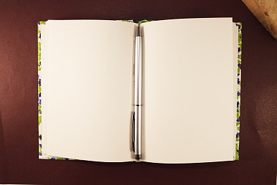 钢笔和记事本孤立在皮革背景上。棕色皮革上的钢笔和笔记本。从以上观点。它是新闻、诗歌、作家和创造者的象征。图片下载