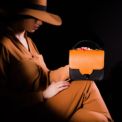 穿着西装的年轻女子坐着，拿着黑色背景上的棕色和黑色皮包图片下载