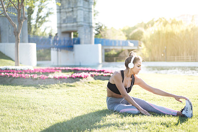 运动妇女做草坪运动和伸展在户外的草地上在公园听音乐图片下载