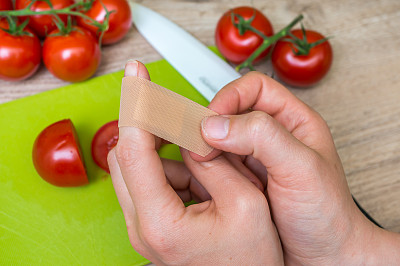 一位妇女在厨房里给她的手指受伤处敷上创可贴图片下载