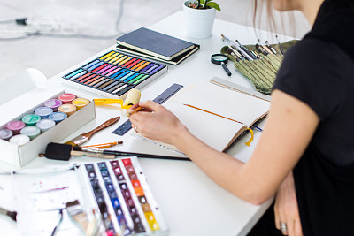 一个女性画家用铅笔在素描簿上画草稿的特写角度视图。艺术家素描在艺术工作室与蜡笔集。图片下载