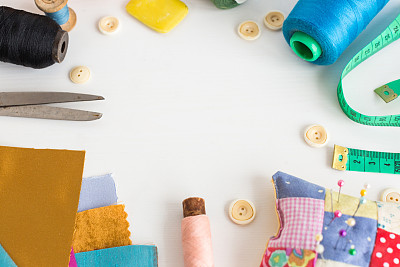 刺绣，工艺，缝纫和裁剪概念-工具近距离在白色的桌子上，测量米，粉色，蓝色和黑色的线轴，彩色织物的碎片，大头针和针垫，白色纽扣，肥皂图片下载
