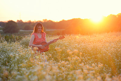 在野花地里拿着吉他的女人。图片下载