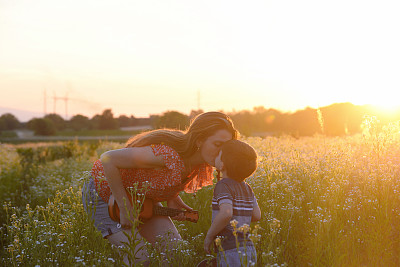 在日落的草地上，妈妈亲吻着她的小男孩。图片下载
