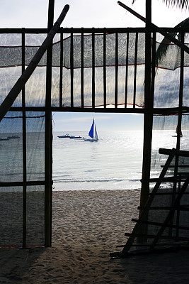 海滩上的栅栏和夕阳下漂流的帆船图片下载