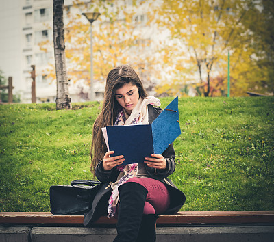 女学生在公园长凳上做作业。图片下载