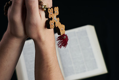 年轻的基督徒祈祷手与木制的念珠和圣经孤立在黑色的背景。图片下载