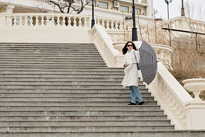 年轻女子身穿白大褂，撑着伞走下楼梯。图片下载