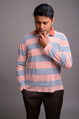 在灰色背景下，一名年轻的印度男子穿着条纹长袖图片下载