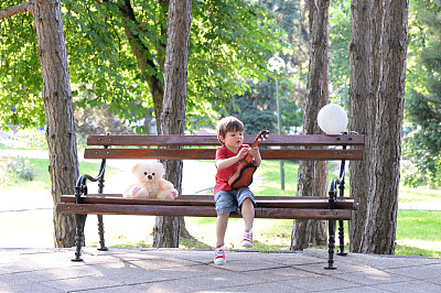 小男孩在公园的长椅上弹吉他图片下载