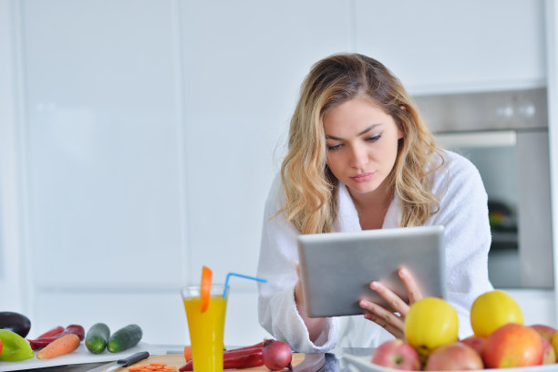 笑容可掬的美女在早餐时准备沙拉。照片中的年轻女子在浴衣。饮食。健康的生活方式图片下载