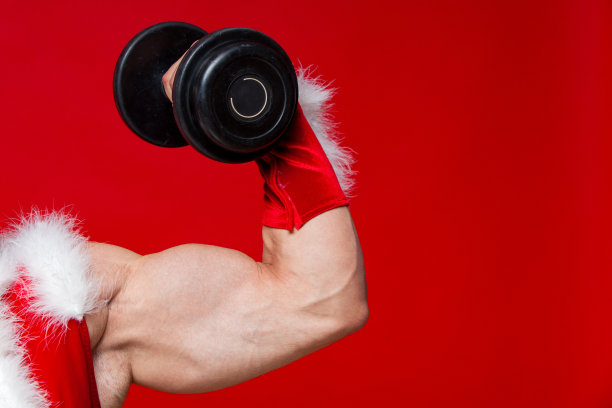 节日和庆祝活动，新年，圣诞节，体育，健身，健康的生活方式-肌肉英俊性感的圣诞老人。孤立在红色背景上。显示了一个大的二头肌。特写镜头图片下载