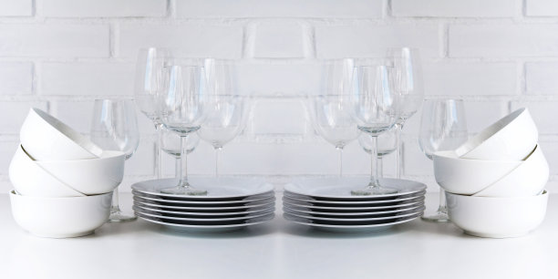 白色餐具堆放在木桌上，背景是白色，还有透明的酒杯。副本的空间。图片下载