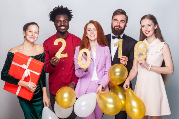 穿着漂亮的人庆祝新年。拿着礼盒，彩色气球和数字2018，看着相机微笑。图片下载