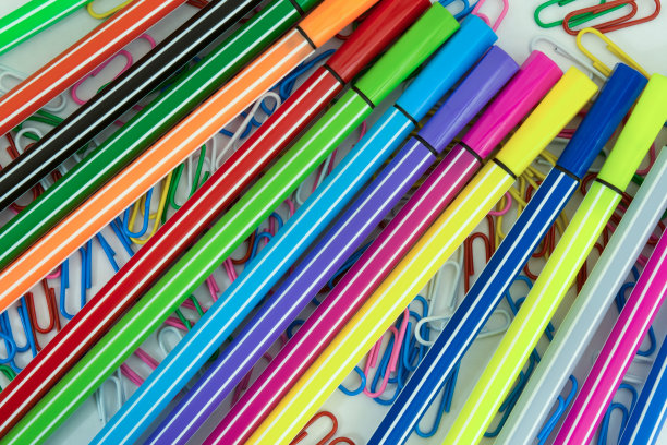 不同颜色的回形针和记号笔随意地散落在白纸上图片下载
