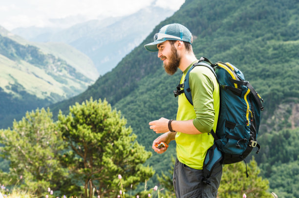 在高加索山脉的背景下，一个年轻的旅行者的肖像，留着胡子，背着背包，戴着帽子和太阳镜图片下载