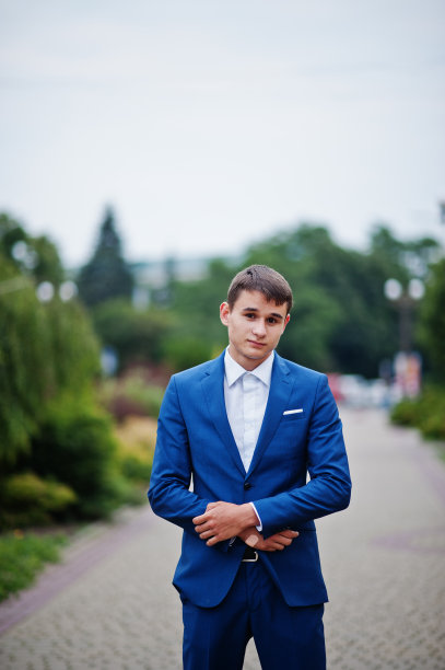 一幅帅气的年轻人的肖像，穿着正式的奇装妙服，在公园的人行道上摆姿势。图片下载