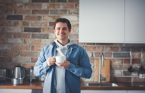 英俊的男人拿着一杯茶或咖啡站在厨房图片下载