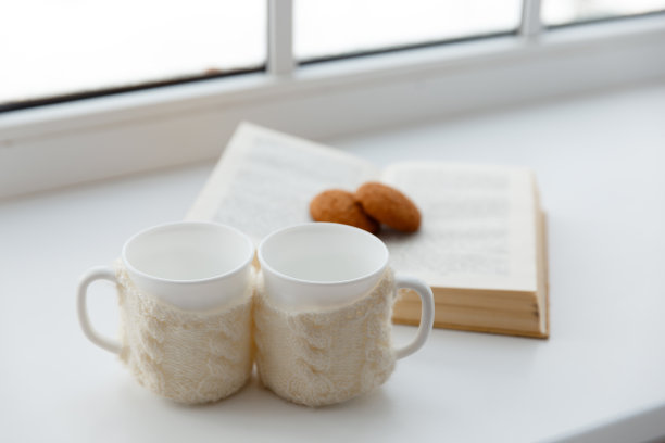 在一扇窗户后面的桌子上放着两个围着围巾的白杯子图片下载