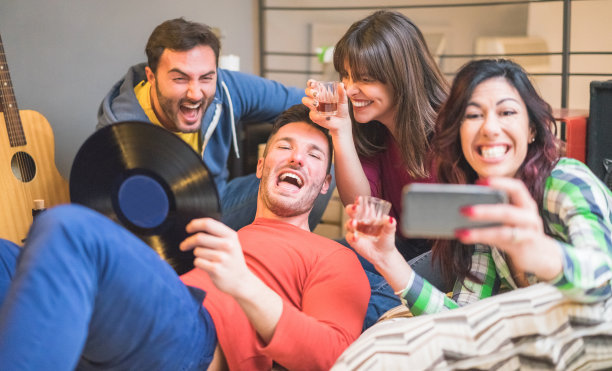 快乐的朋友与智能手机相机自拍照片在青年旅舍聚会-年轻人一起喝酒和有乐趣-聚焦左女人的脸-友谊，音乐和聚会的概念图片下载