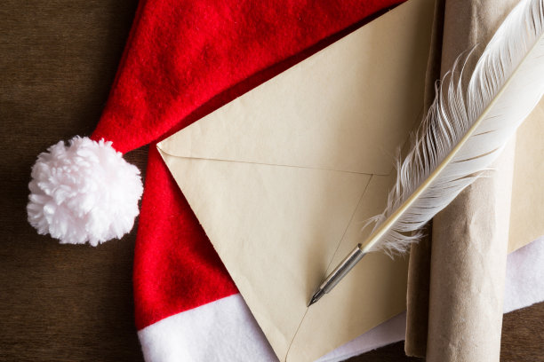 红色帽子上的旧信封、纸卷和羽毛笔：孩子们和成年人写给圣诞老人的信。圣诞节的概念。顶视图。素材图片