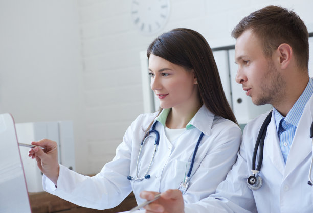 两位医生在办公室开会时一起讨论新的治疗方法的照片。医生一边使用台式电脑一边讨论新的治疗方法。图片下载