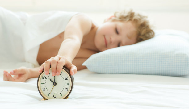 男孩的手伸向闹钟，想把它关掉。图片下载