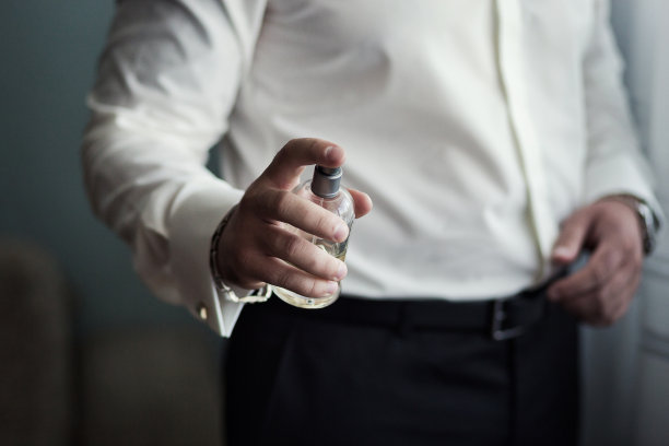 英俊的男人选择香水，富有的男人喜欢昂贵的古龙水，优雅的男人在西装上使用古龙水或香水，男性香水，成功的商人喜欢香水味图片下载